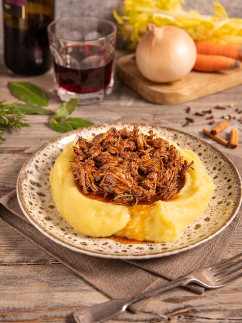 Stracotto di manzo sfilacciato con sugo scuro servito su letto di purè di patate
