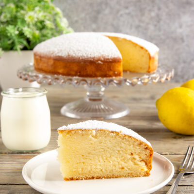 Torta allo yogurt senza uova a fette, soffice e spolverata di zucchero a velo, con limoni freschi accanto