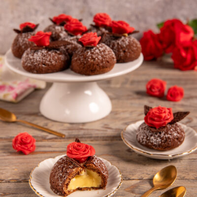 Bignè craqueline al cioccolato ripieni di crema zabaione, aperti a metà e decorati con rose di cioccolato