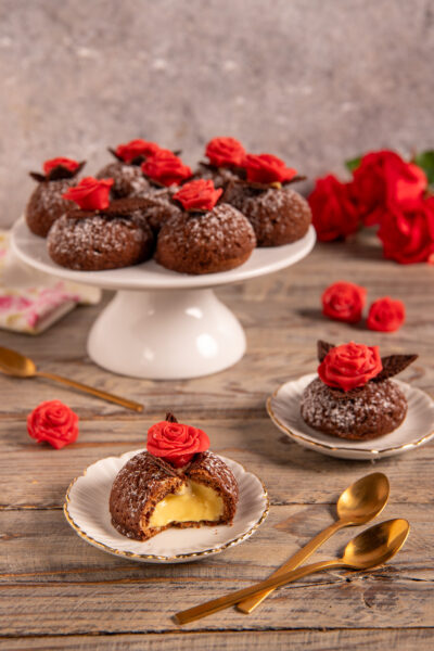 Bignè craqueline al cioccolato ripieni di crema zabaione, aperti a metà e decorati con rose di cioccolato