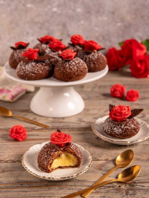 Bignè craqueline al cioccolato ripieni di crema zabaione, aperti a metà e decorati con rose di cioccolato