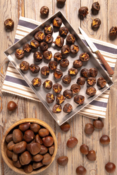 Castagne al forno con incisione a croce su teglia, affiancate da castagne crude