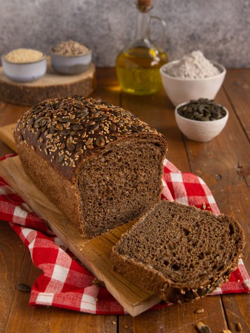 Pane nero in cassetta a fette con crosta ricoperta di semi misti e mollica scura alveolata