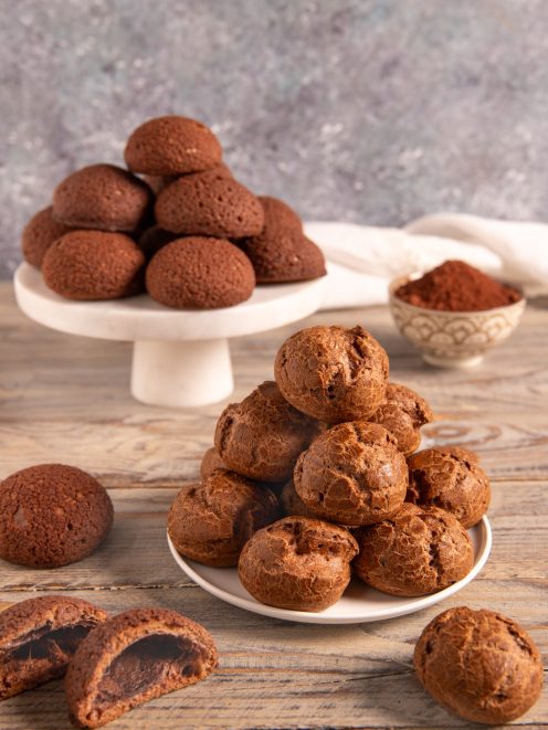 Bignè al cacao dalla superficie craquelée impilati su un piatto, con uno tagliato a mostrare il cuore vuoto