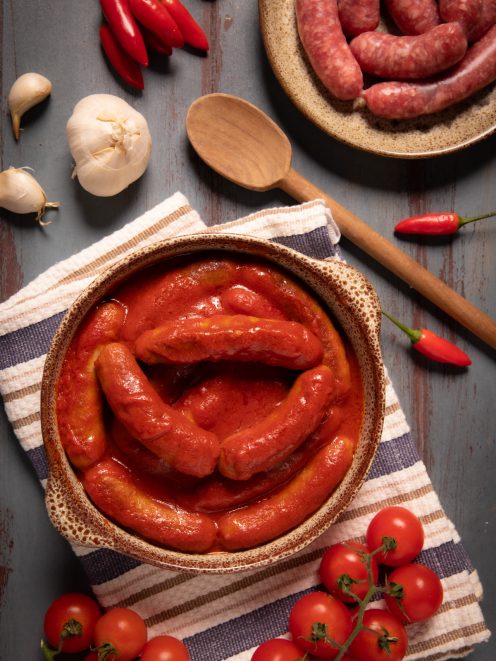 Salsiccia al sugo immersa in una salsa di pomodoro densa, servita con peperoncini e aglio