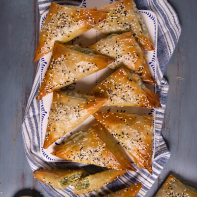 Spanakopita: triangoli di pasta fillo dorati con ripieno di spinaci e semi di sesamo bianco e nero