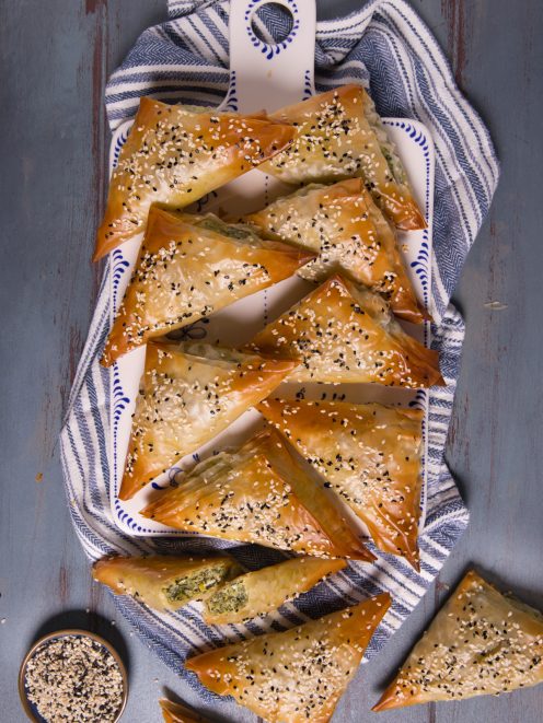 Spanakopita: triangoli di pasta fillo dorati con ripieno di spinaci e semi di sesamo bianco e nero