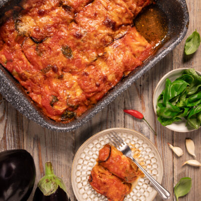 Cannelloni di melanzane al forno con salsa di pomodoro e basilico, serviti nel tegame e in un piatto