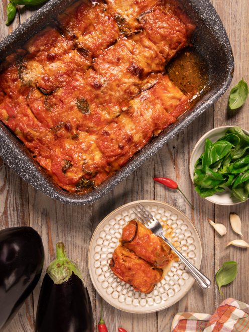 Cannelloni di melanzane al forno con salsa di pomodoro e basilico, serviti nel tegame e in un piatto