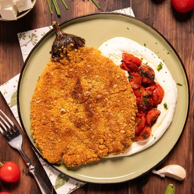 Cotoletta di melanzana impanata e dorata su crema bianca con pomodorini saltati e erbe fresche