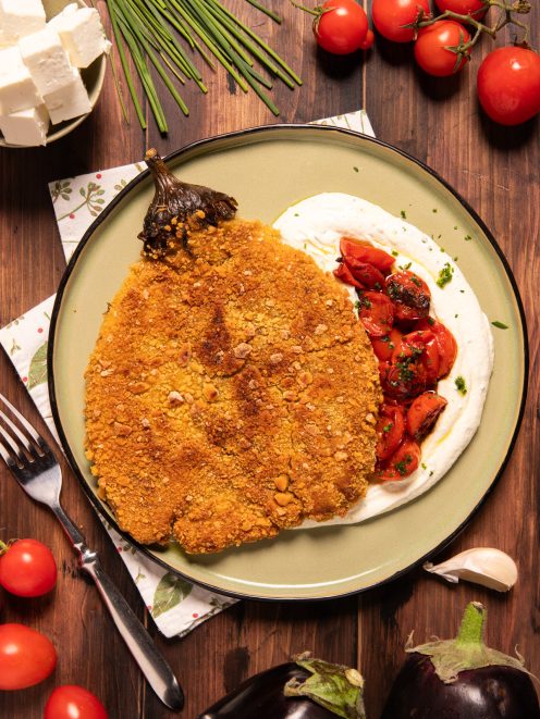 Cotoletta di melanzana impanata e dorata su crema bianca con pomodorini saltati e erbe fresche