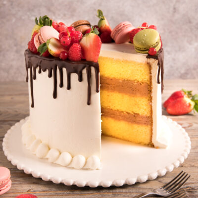 Drip cake con strati di pan di spagna e crema, glassa al cioccolato e frutti di bosco freschi