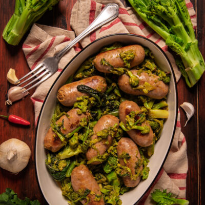 Salsiccia e friarielli serviti in un piatto ovale, con le salsicce dorate adagiate sulle cime di rapa saltate