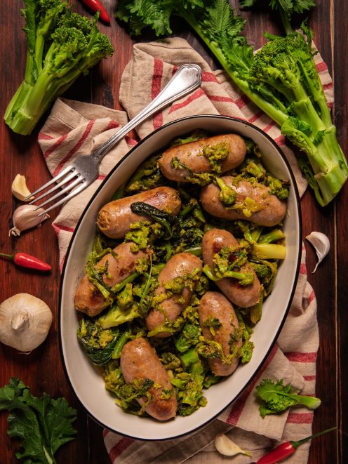 Salsiccia e friarielli serviti in un piatto ovale, con le salsicce dorate adagiate sulle cime di rapa saltate