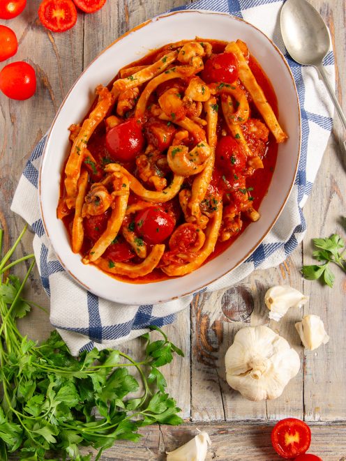 Seppie in umido con pomodorini interi e sugo rosso, guarnite con prezzemolo tritato