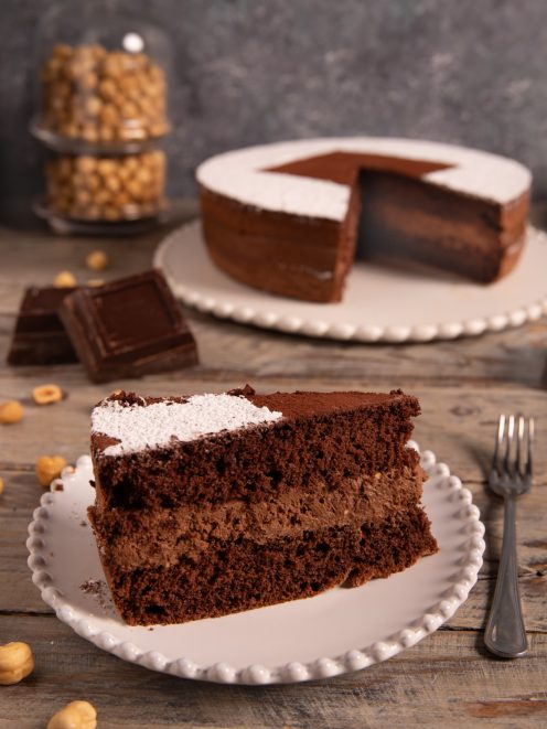 Torta cioccolato e nocciole in sezione, con strato di crema e zucchero a velo sulla superficie