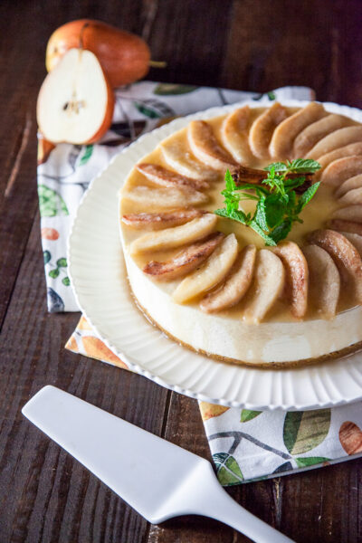 Cheesecake senza glutine con spicchi di pere caramellate disposti a raggiera e stecca di cannella al centro