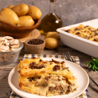 Parmigiana di patate, funghi e salsiccia a strati filanti servita in una fetta dorata