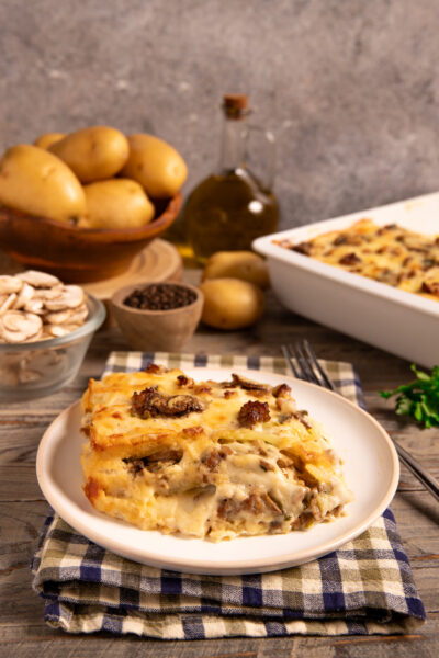 Parmigiana di patate, funghi e salsiccia a strati filanti servita in una fetta dorata