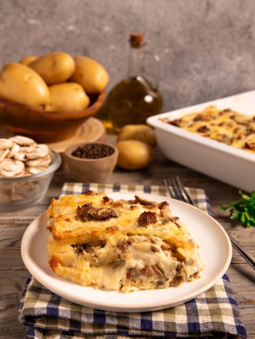 Parmigiana di patate, funghi e salsiccia a strati filanti servita in una fetta dorata