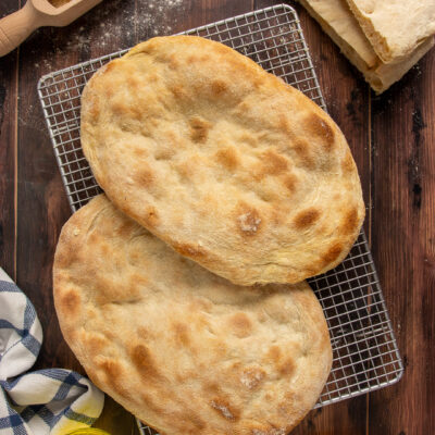 Pinsa romana appena sfornata con crosta dorata e alveolatura aperta, servita intera e tagliata