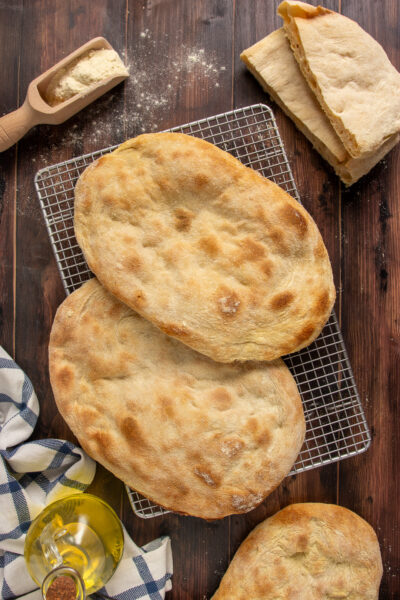Pinsa romana appena sfornata con crosta dorata e alveolatura aperta, servita intera e tagliata