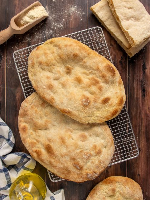 Pinsa romana appena sfornata con crosta dorata e alveolatura aperta, servita intera e tagliata