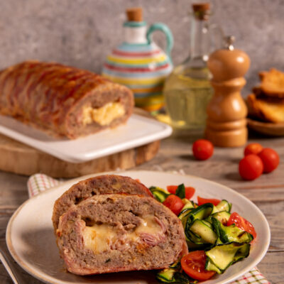 Polpettone di carne vestito affettato con ripieno di formaggio e salume, servito con zucchine e pomodorini