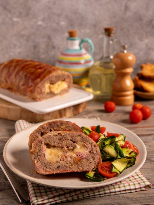 Polpettone di carne vestito affettato con ripieno di formaggio e salume, servito con zucchine e pomodorini