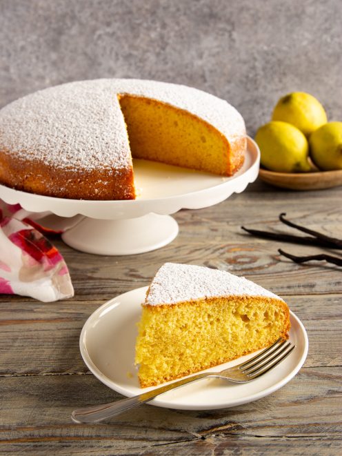 Torta all'acqua spolverata di zucchero a velo, con una fetta tagliata che mostra la mollica soffice e dorata