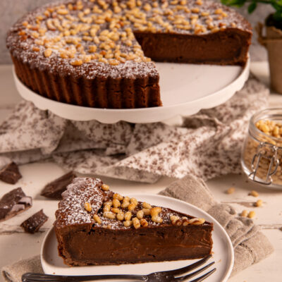 Torta della nonna al cioccolato con pinoli caramellati e zucchero a velo, tagliata a fette