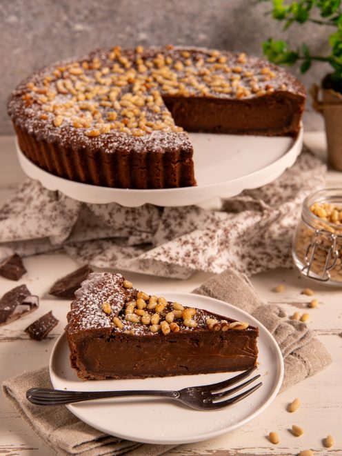 Torta della nonna al cioccolato con pinoli caramellati e zucchero a velo, tagliata a fette