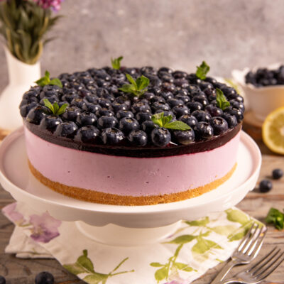 Torta fredda yogurt e mirtilli con base di biscotto, mousse rosa e copertura di mirtilli freschi e menta
