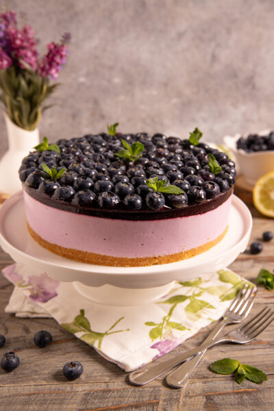 Torta fredda yogurt e mirtilli con base di biscotto, mousse rosa e copertura di mirtilli freschi e menta