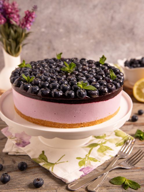 Torta fredda yogurt e mirtilli con base di biscotto, mousse rosa e copertura di mirtilli freschi e menta