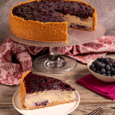 Cheesecake ai mirtilli con base di biscotto, farcitura cremosa e gelatina di mirtilli, servita a fetta