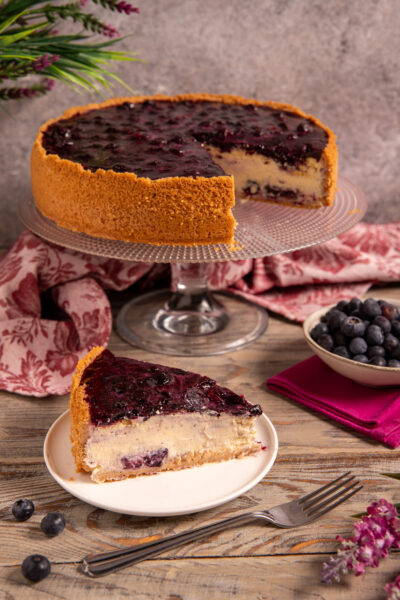 Cheesecake ai mirtilli con base di biscotto, farcitura cremosa e gelatina di mirtilli, servita a fetta