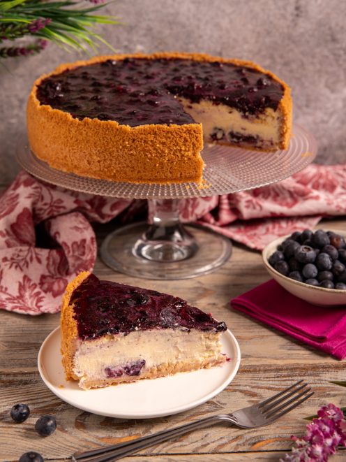 Cheesecake ai mirtilli con base di biscotto, farcitura cremosa e gelatina di mirtilli, servita a fetta