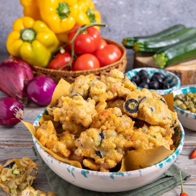 Cecamariti fritti con olive nere in ciotola, circondati da verdure fresche e peperoncini