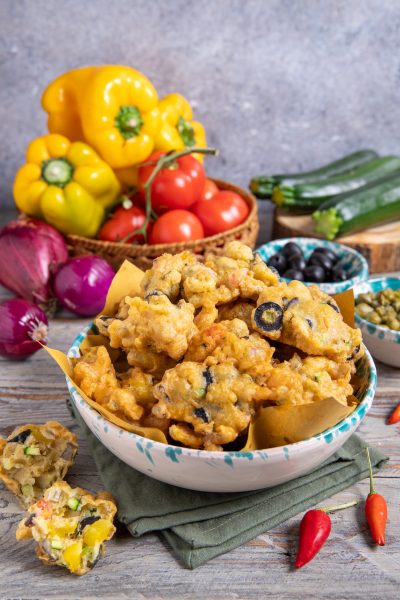 Cecamariti fritti con olive nere in ciotola, circondati da verdure fresche e peperoncini