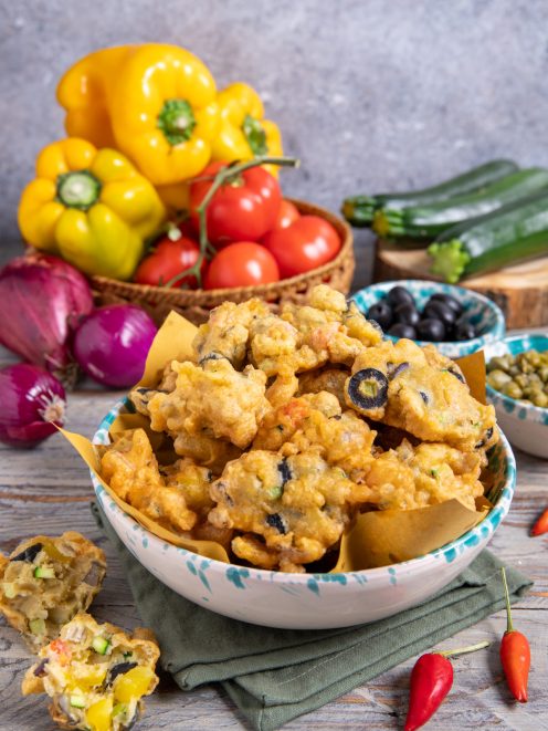 Cecamariti fritti con olive nere in ciotola, circondati da verdure fresche e peperoncini