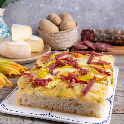 Focaccia con patate, fiori di zucca e salame di Varzi tagliata a fette su vassoio