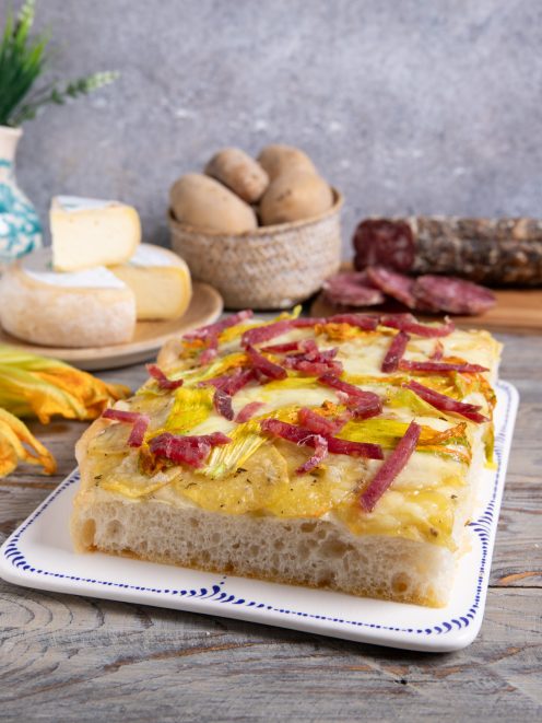 Focaccia con patate, fiori di zucca e salame di Varzi tagliata a fette su vassoio