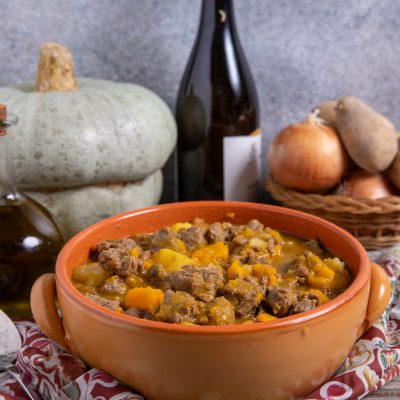 Spezzatino con patate e zucca servito in tegame di terracotta con sugo dorato
