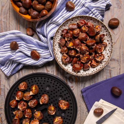 Castagne al microonde con guscio inciso, pronte da cuocere su teglia forata accanto a castagne crude