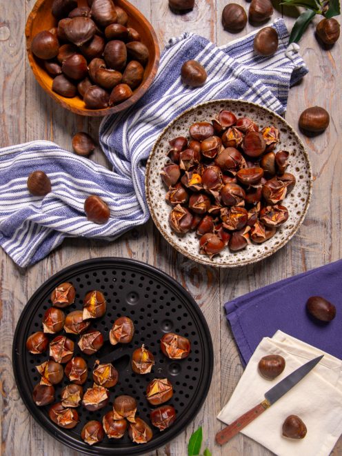 Castagne al microonde con guscio inciso, pronte da cuocere su teglia forata accanto a castagne crude