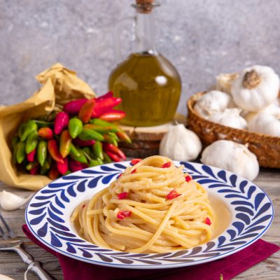 Spaghetti con crema di aglio e peperoncino arrotolati nel piatto e conditi con peperoncino a pezzetti