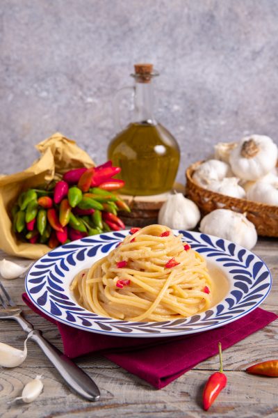 Spaghetti con crema di aglio e peperoncino arrotolati nel piatto e conditi con peperoncino a pezzetti