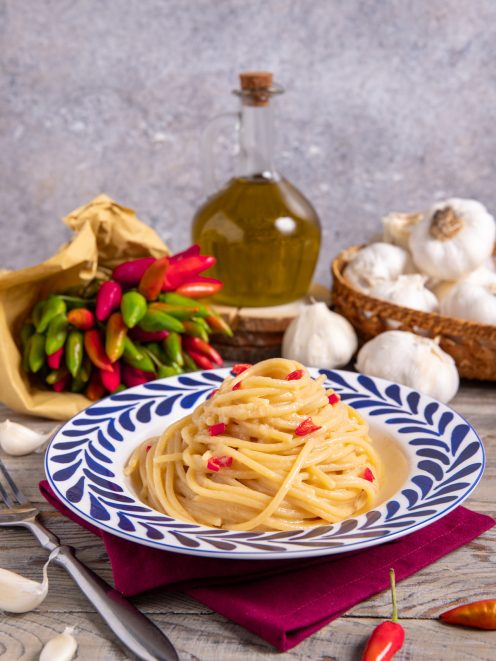 Spaghetti con crema di aglio e peperoncino arrotolati nel piatto e conditi con peperoncino a pezzetti