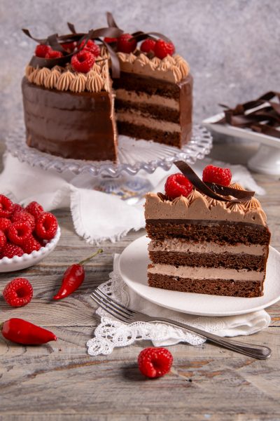 Torta al doppio cioccolato e peperoncino a strati, fetta con crema al cioccolato e lamponi